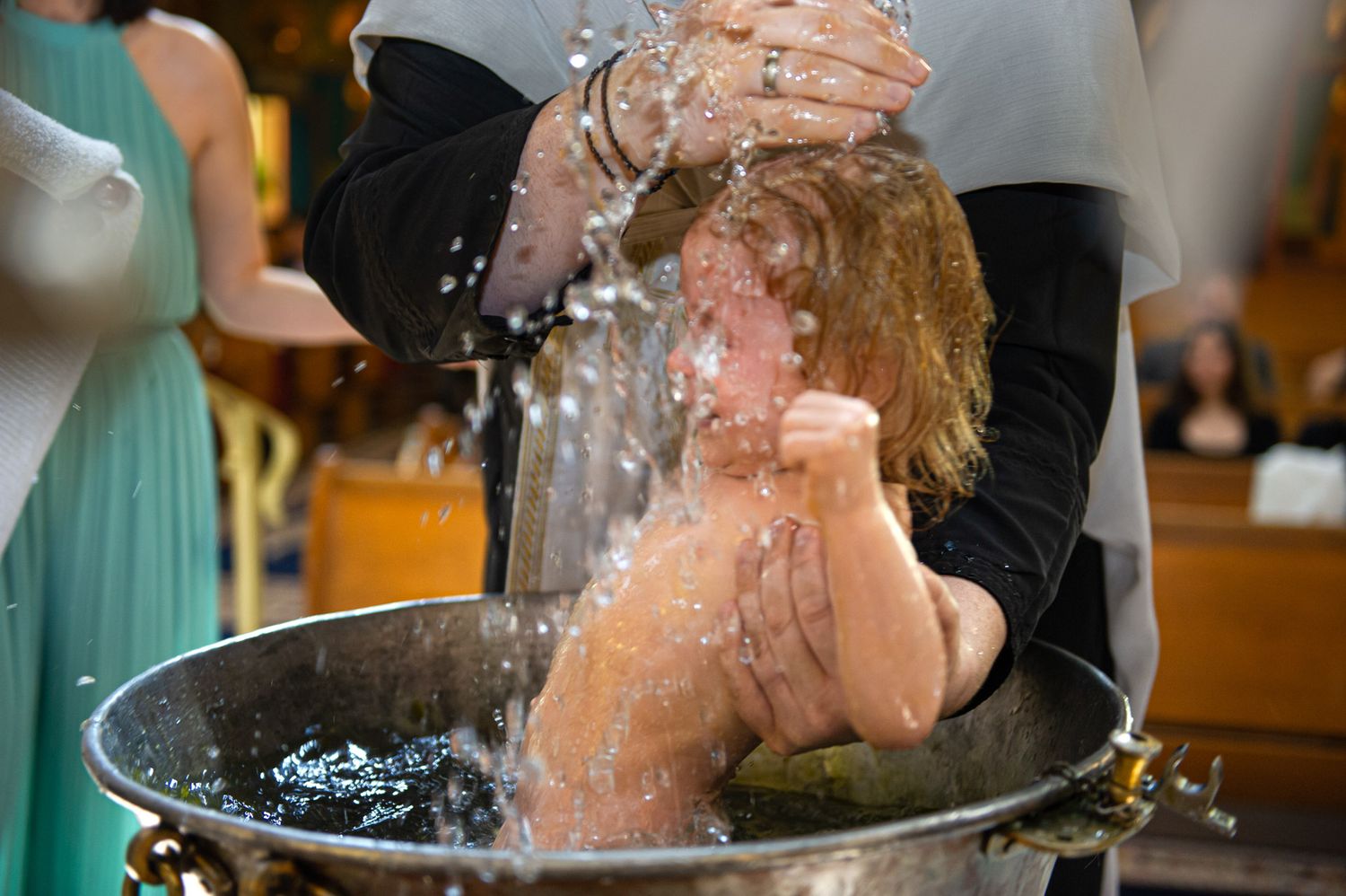 Baby being baptized with water poured over head in baptismal font.
