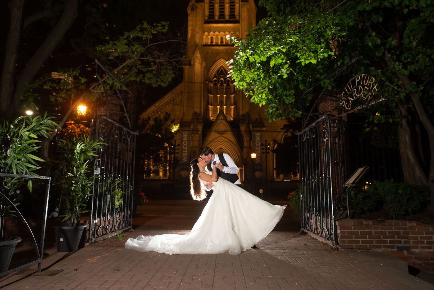 Couple shares romantic dip kiss outside illuminated historic church at night in Downtown Toronto.