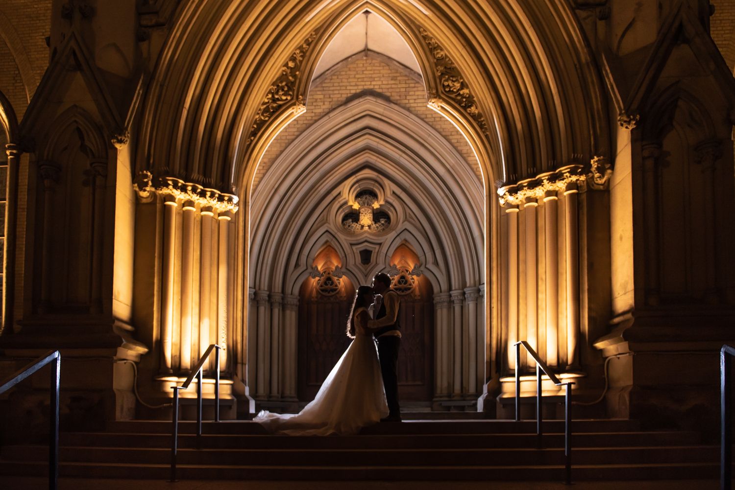 Bride and groom silhouetted in glowing Catholic church entrance at night in Downtown Toronto.