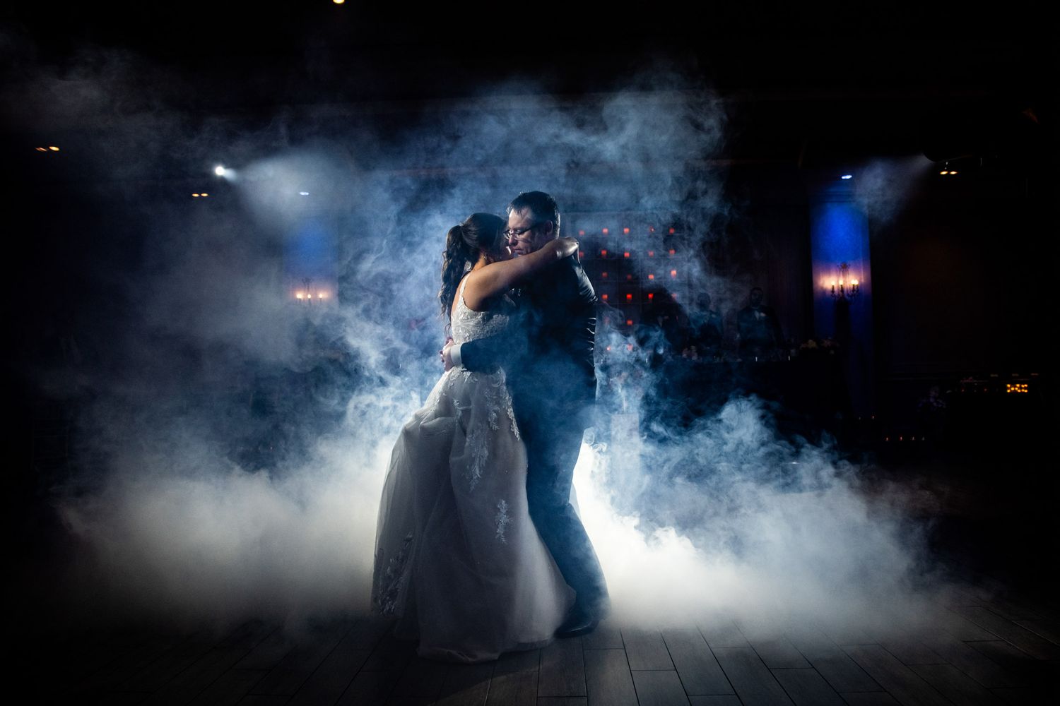 Bride and groom share romantic first dance surrounded by dramatic fog and blue lighting at wedding reception in Parkview Manor Banquet Hall.