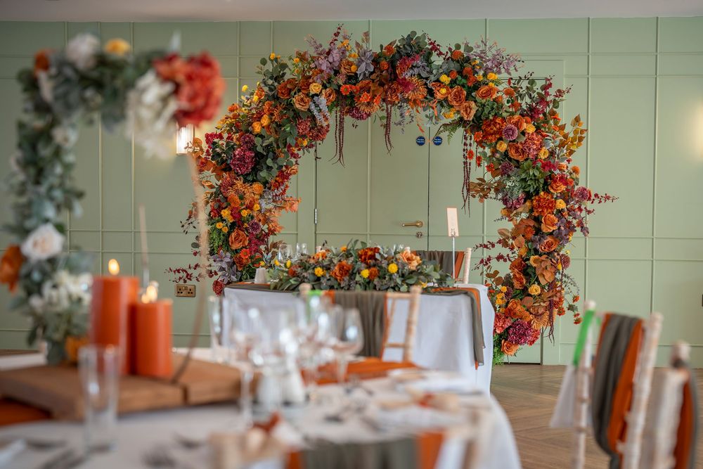 Wedding reception tables decorated with vibrant orange and red floral arrangements.