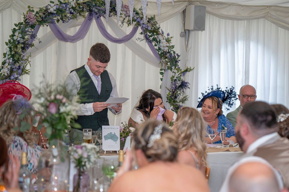 Wedding reception speech being delivered in a decorated marquee with purple and floral decor.