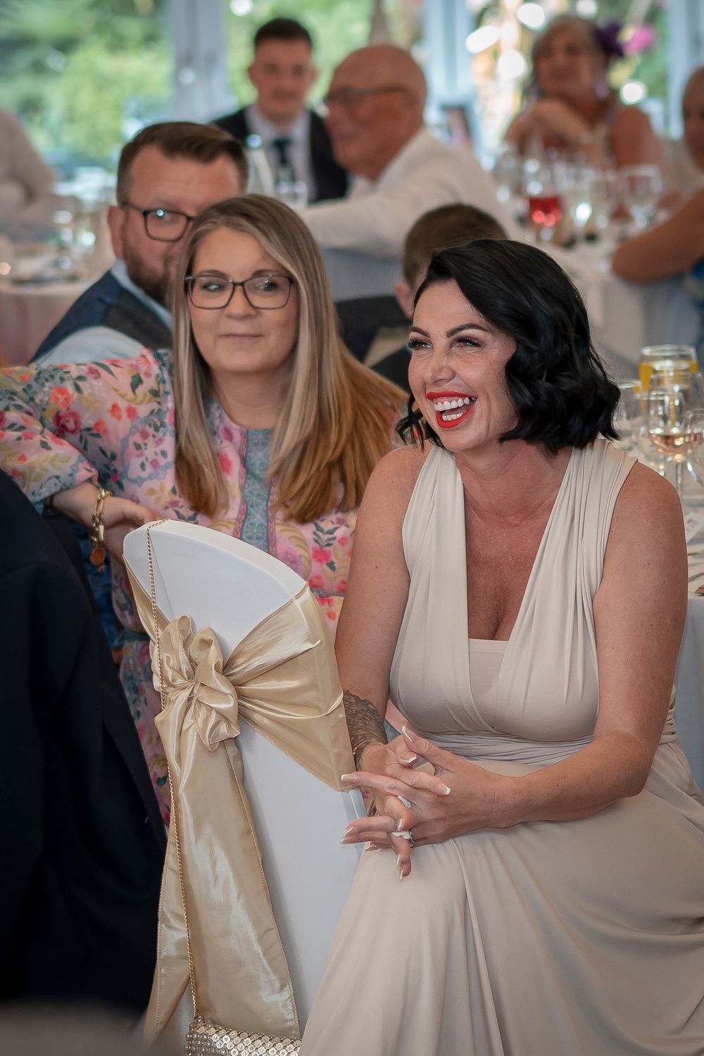 Wedding guests in formal attire seated at decorated reception tables with floral centerpieces.