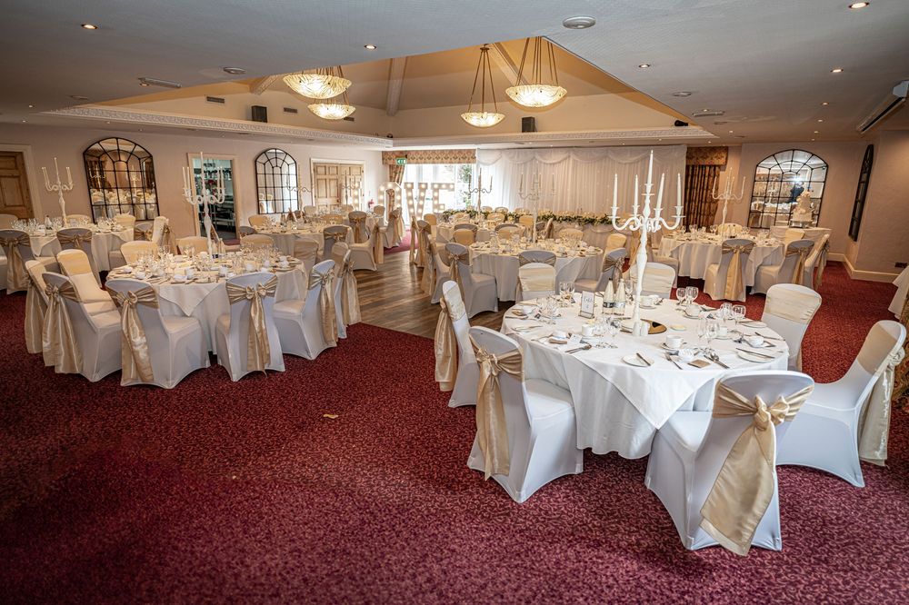 Spacious banquet hall set up with round tables and white chair covers for a formal wedding reception.