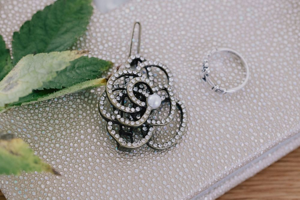 Elegant crystal floral brooch and diamond ring displayed on a gray textured surface with greenery.