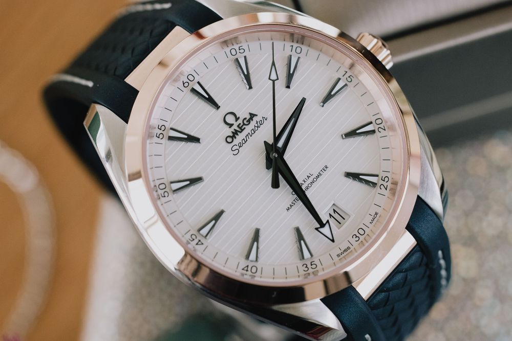 Omega Aqua Terra luxury watch with white dial and teal rubber strap on display.