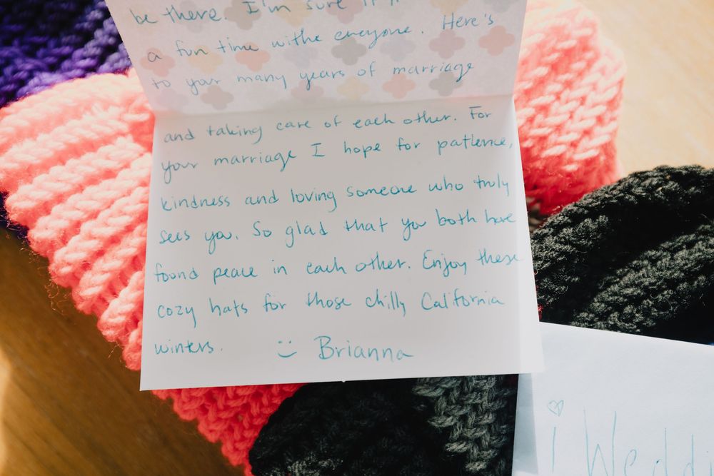 Handwritten wedding card note placed on colorful knitted hats, a heartfelt gift for the newlyweds.