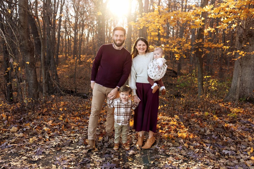 Family of four poses together in golden autumn forest during fall family portrait session.