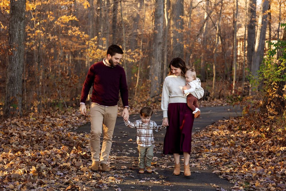 Family of four walks together on leaf-covered path during warm golden fall family photo session.