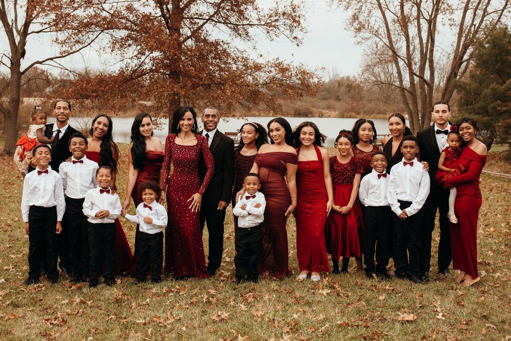 Large extended family in coordinating red and black formal attire poses outdoors in autumn setting.