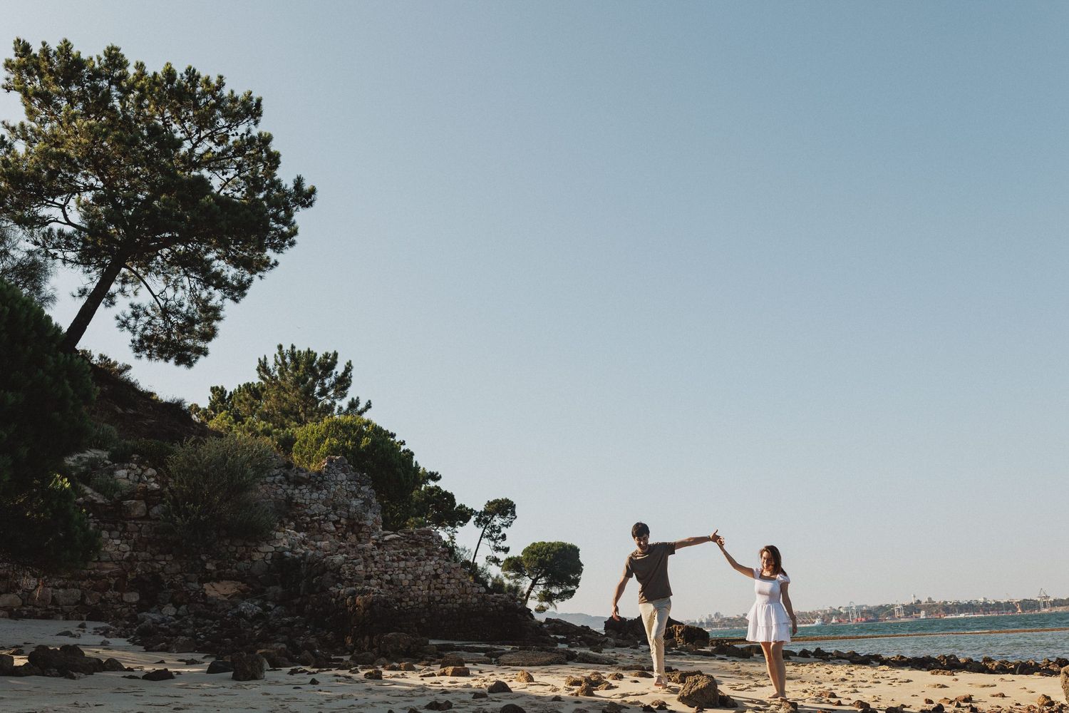 Couple walking barefoot on the beach during engagement photoshoot in Tróia Portugal