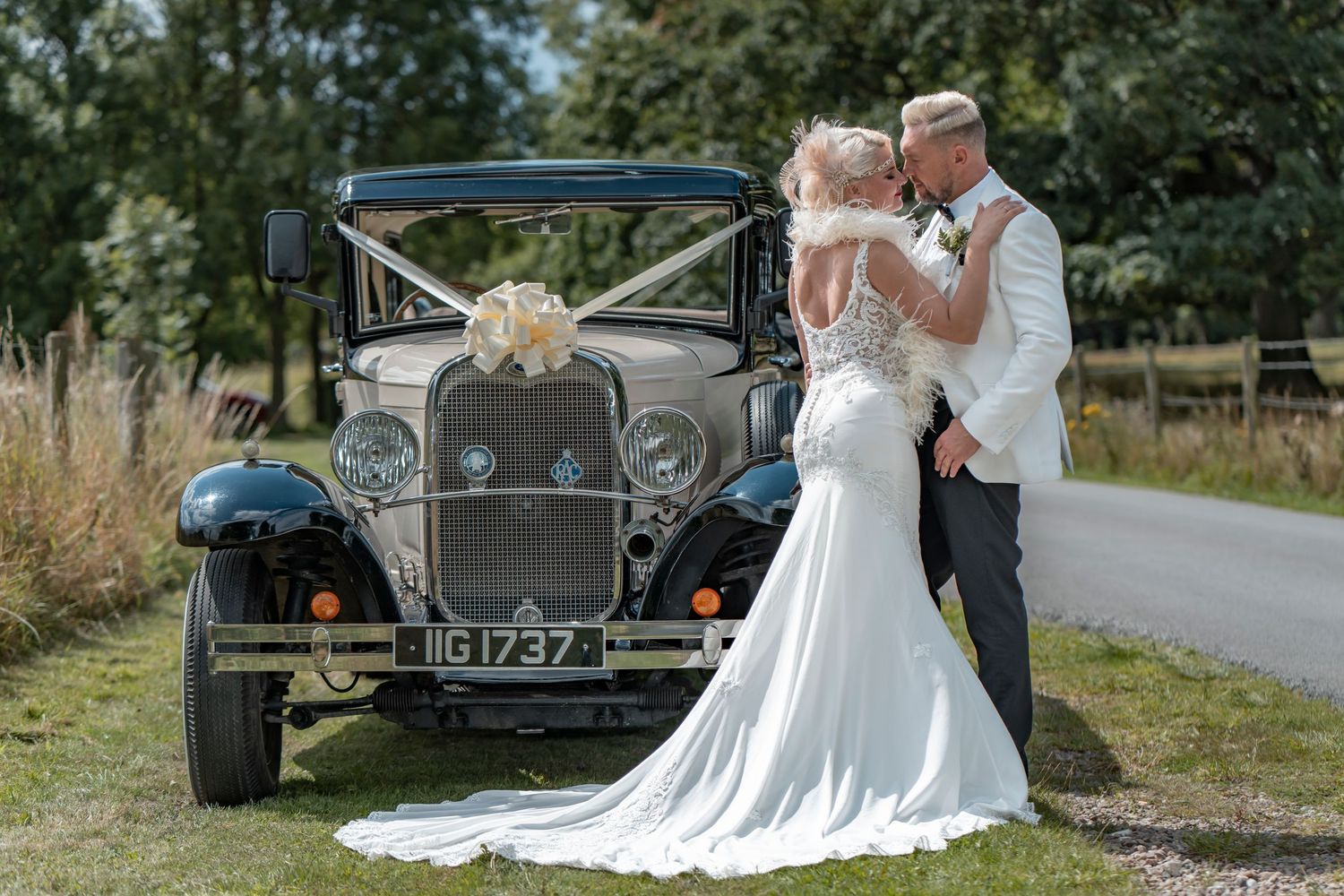 Couple poses with vintage classic car during outdoor wedding photoshoot.