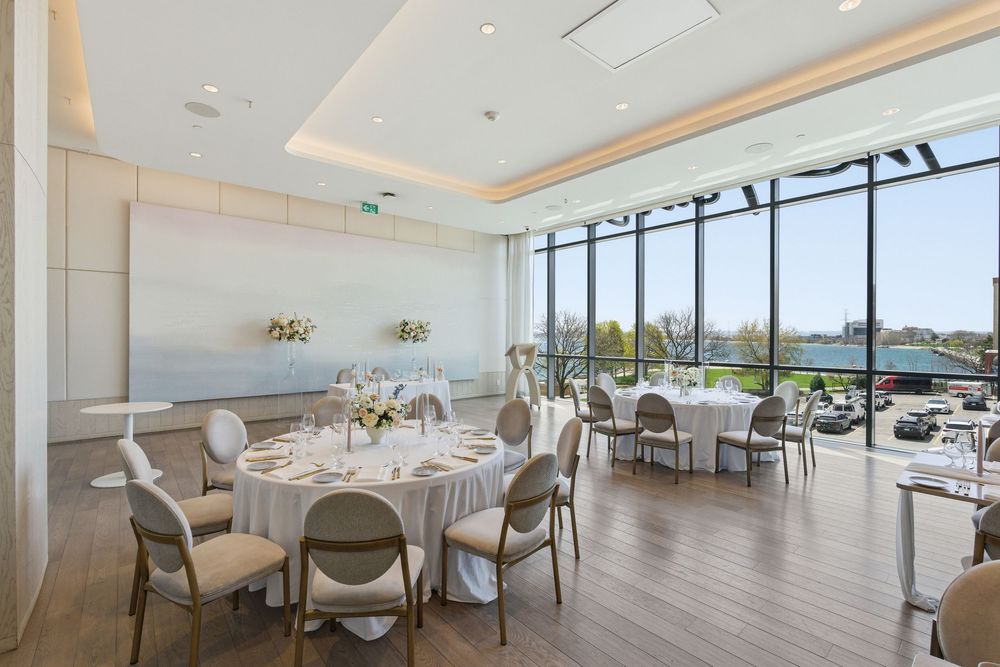 Modern banquet hall with panoramic windows features elegant white table settings and chairs in a bright, minimalist space.