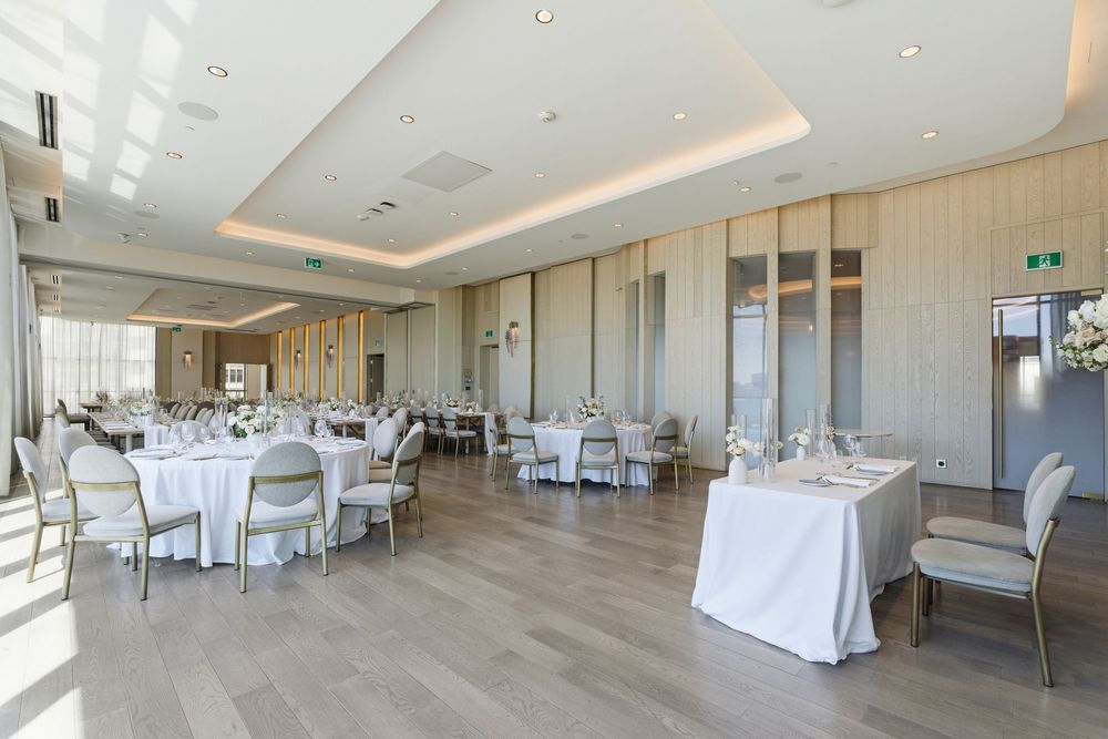 A modern white banquet hall with elegant table settings and recessed lighting in the ceiling.