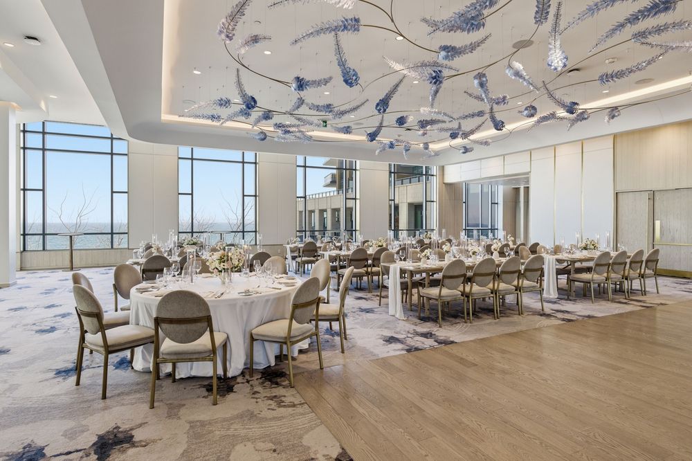 Modern banquet hall interior with blue pendant lights, round tables, and upholstered chairs in an elegant setting.