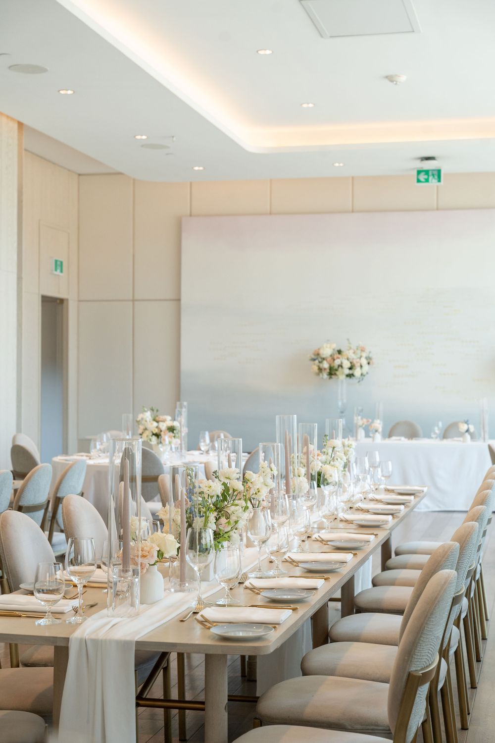 Elegant wedding reception table with white linens, tall candles, and floral centerpieces in a modern banquet room.