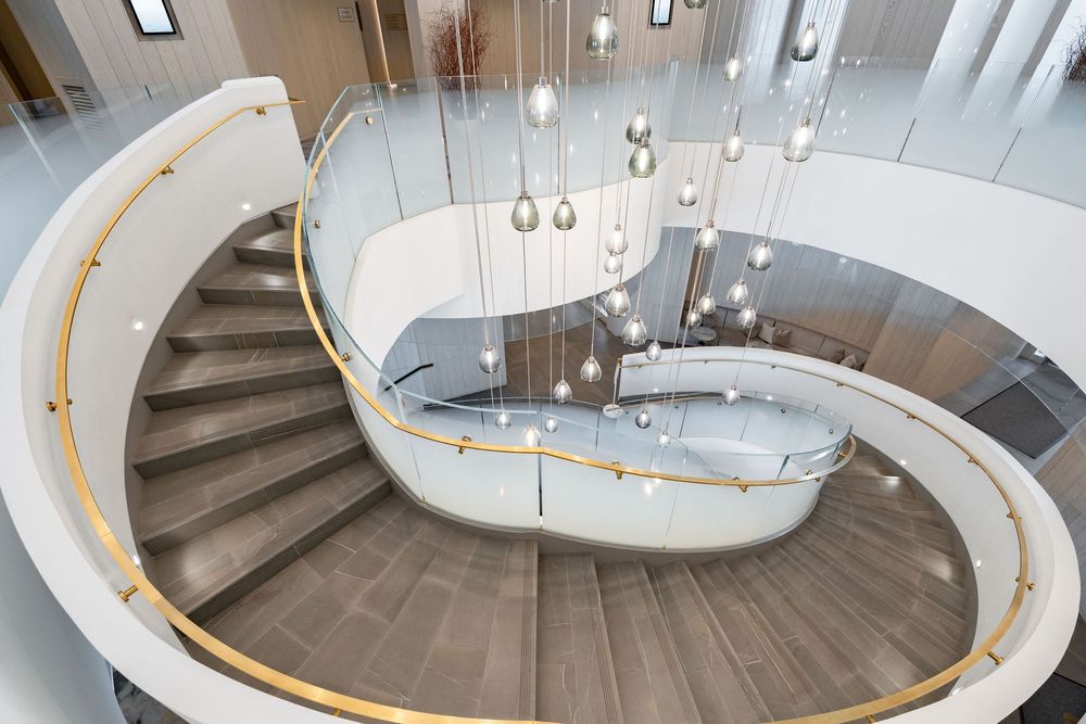 Modern spiral staircase with curved glass railings and hanging pendant lights in a contemporary interior space.