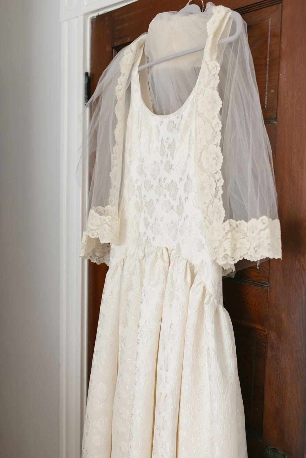 A cream satin wedding dress with a vintage lace veil rests on a wooden oak door. North Shore small, backyard wedding photographer