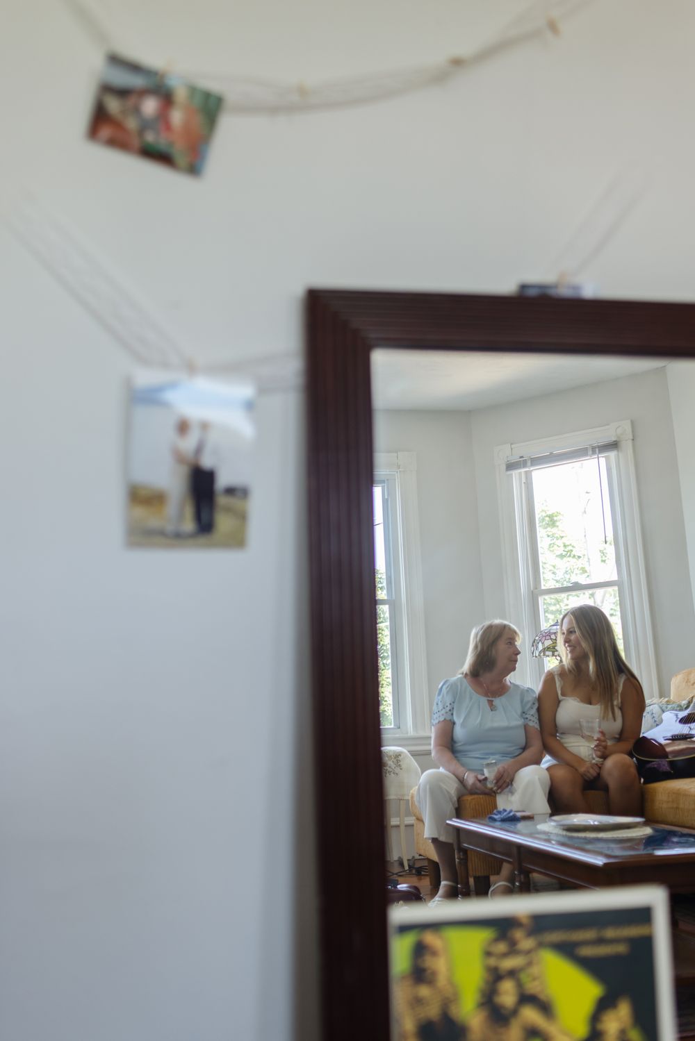 A grandmother and granddaughter look at each other sitting on a couch in a mirror reflecting during getting ready photos in Warren, RI.