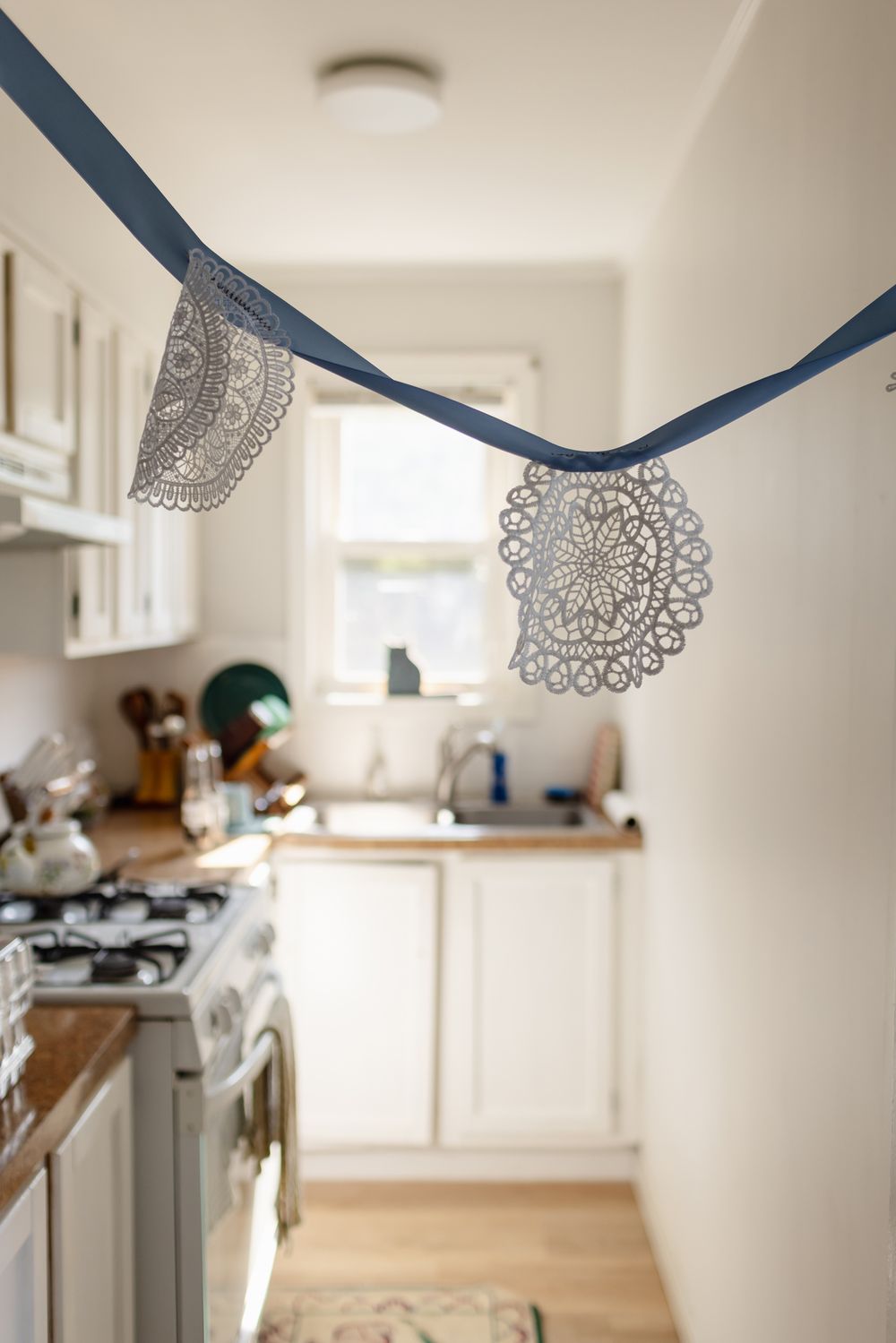 Crochet doilies hang on a blue ribbon in a doorframe of a bright, sunny kitchen in Warren, Rhode Island on a wedding day.