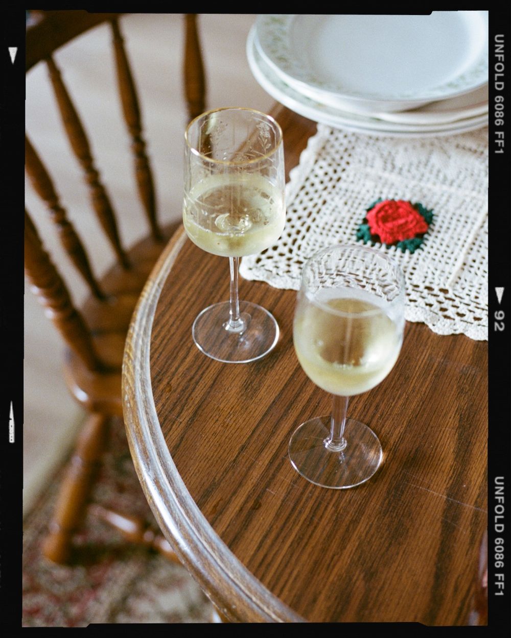 A film photo of wine glasses on a wooden oak table with a crochet piece next to it. Small wedding photographer Newport County Rhode Island.