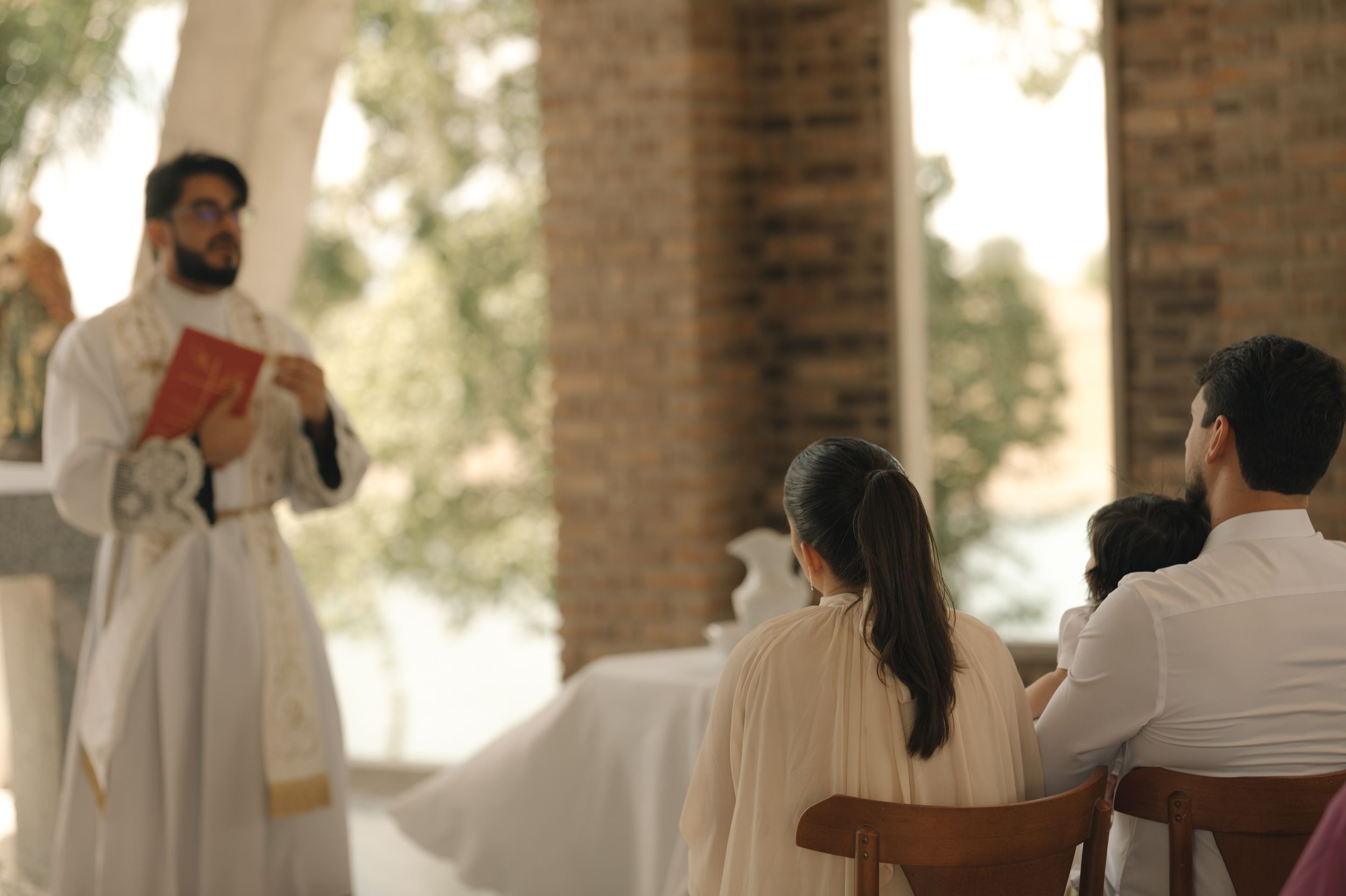 A wedding ceremony takes place in a rustic brick-columned venue with guests seated in white chairs.