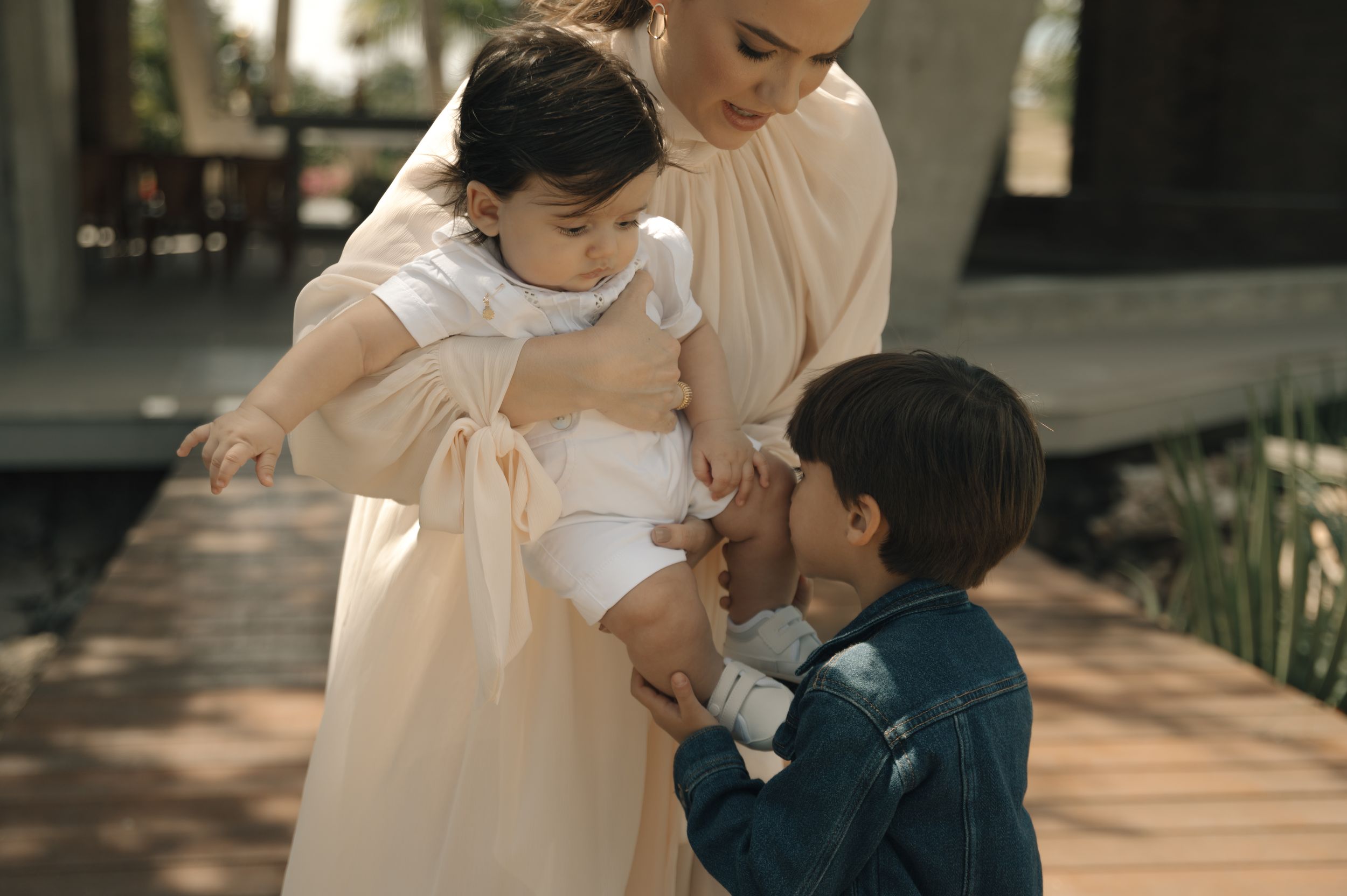 A tender moment captured between parent and child in a sunlit outdoor setting with brick columns.