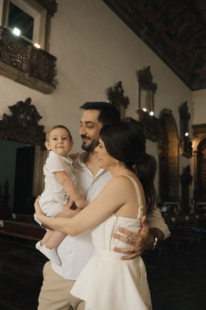 A couple in white attire shares tender moments with their baby during an intimate indoor photoshoot.
