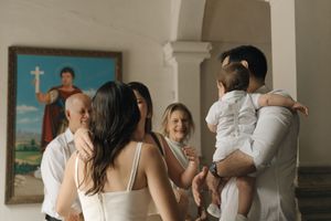 A group gathers inside a church during what appears to be a baptism ceremony, with a cross visible in the background.