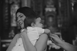 A tender black and white photo shows a person embracing a baby in a white outfit against a dark background.