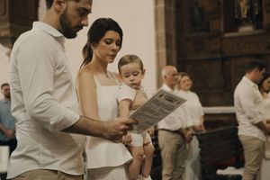 A family in white attire reads a program together at an outdoor event while holding their young child.