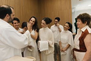 A group of people in white attire stand together in a row against a wooden paneled wall.