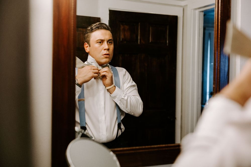 Groom adjusting bow tie while looking at his reflection in a mirror before wedding.