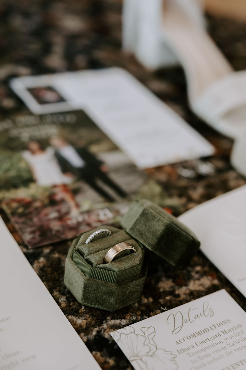 Wedding bands displayed in green velvet ring box alongside wedding invitation suite on table.