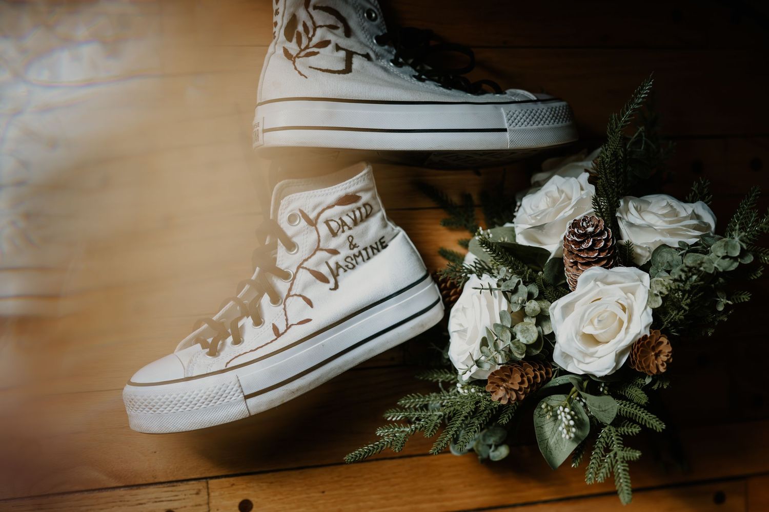 White canvas sneakers and delicate floral bouquet with roses and pine cones arranged for a wedding photoshoot.