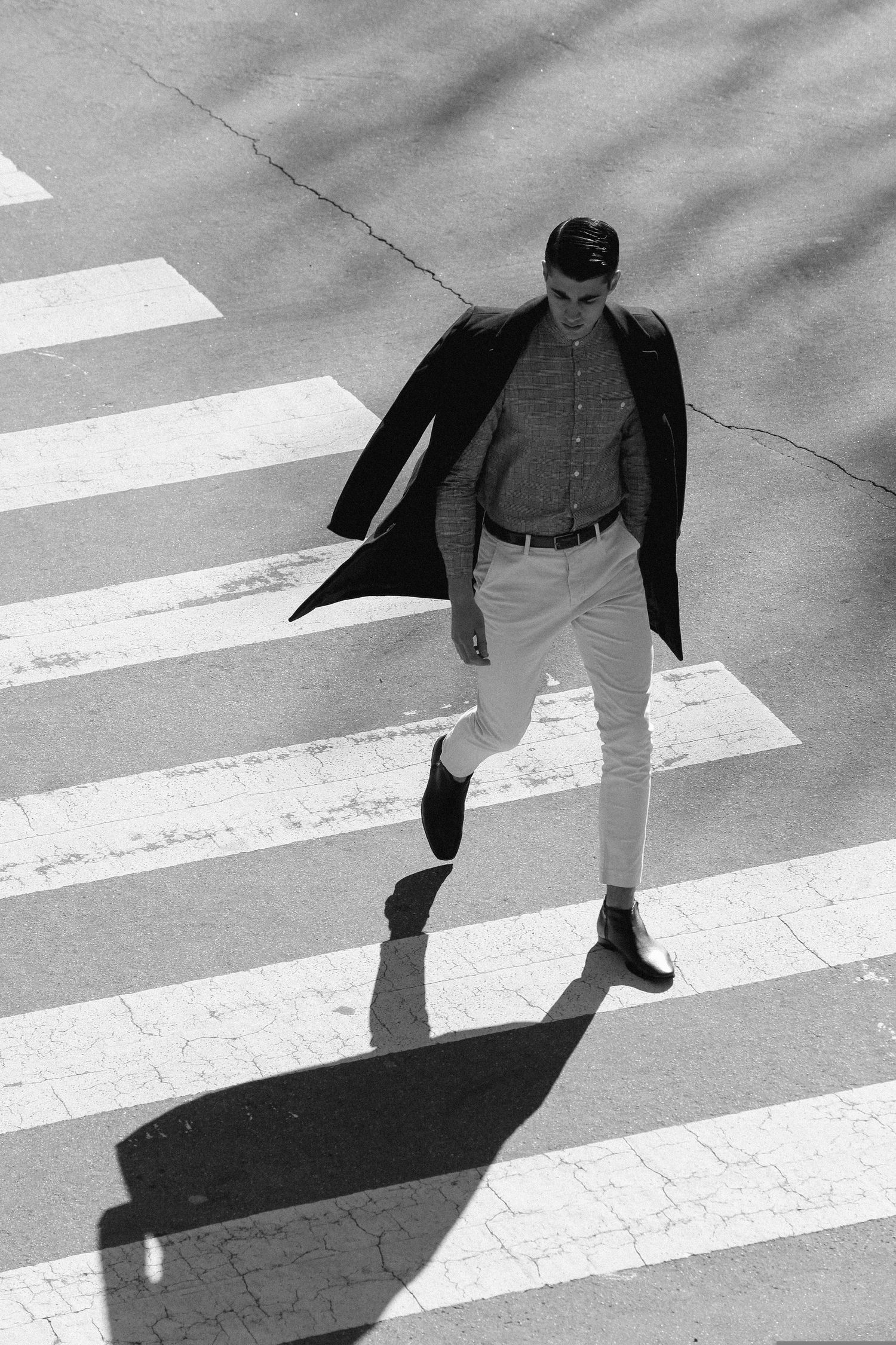 Black and white photograph of a person crossing a pedestrian crosswalk while casting a dramatic shadow on the street.