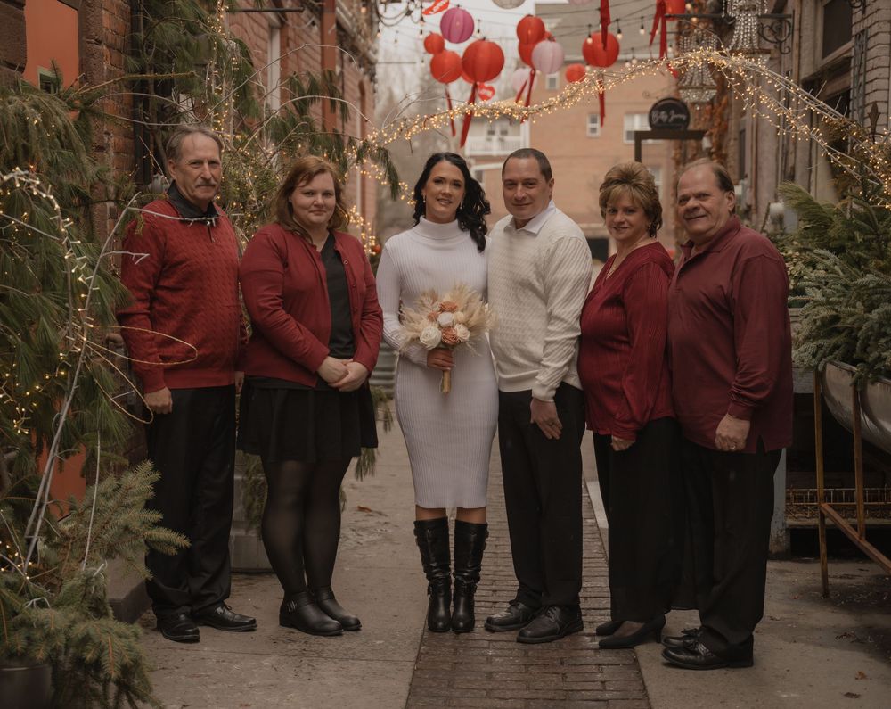Couple in white wedding attire posing with four family members in red in a decorated festive alley.