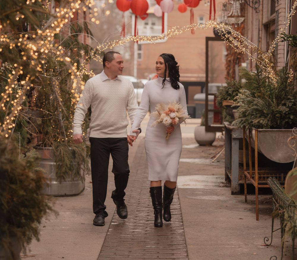 Couple in matching white outfits walking hand-in-hand through a festive alley with string lights and red lanterns.