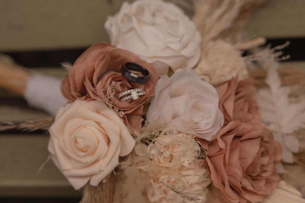Elegant bridal bouquet with blush and cream roses featuring wedding rings nestled among the flowers.