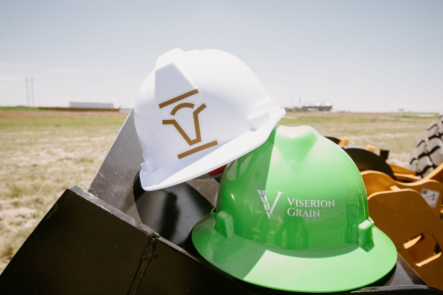 White Five Rivers and green Viserion Grain hard hats resting on construction equipment outdoors.