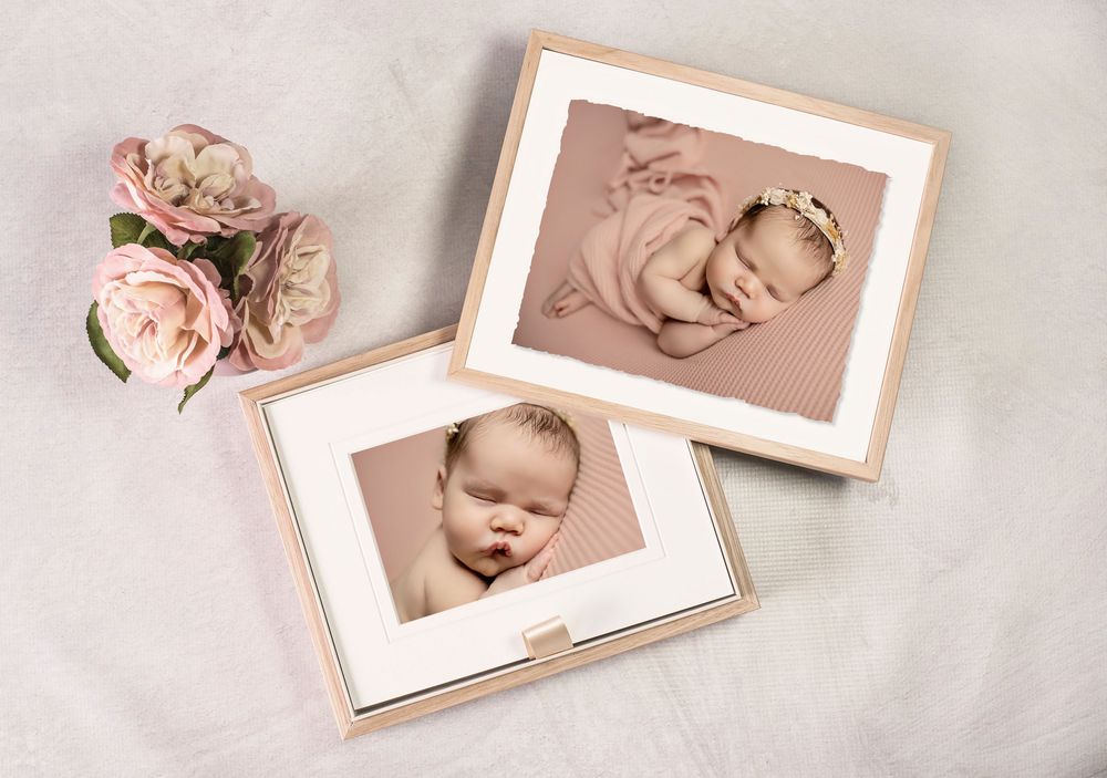 Two framed newborn baby photos displayed with pink roses, showcasing professional infant portrait photography in soft pink tones.