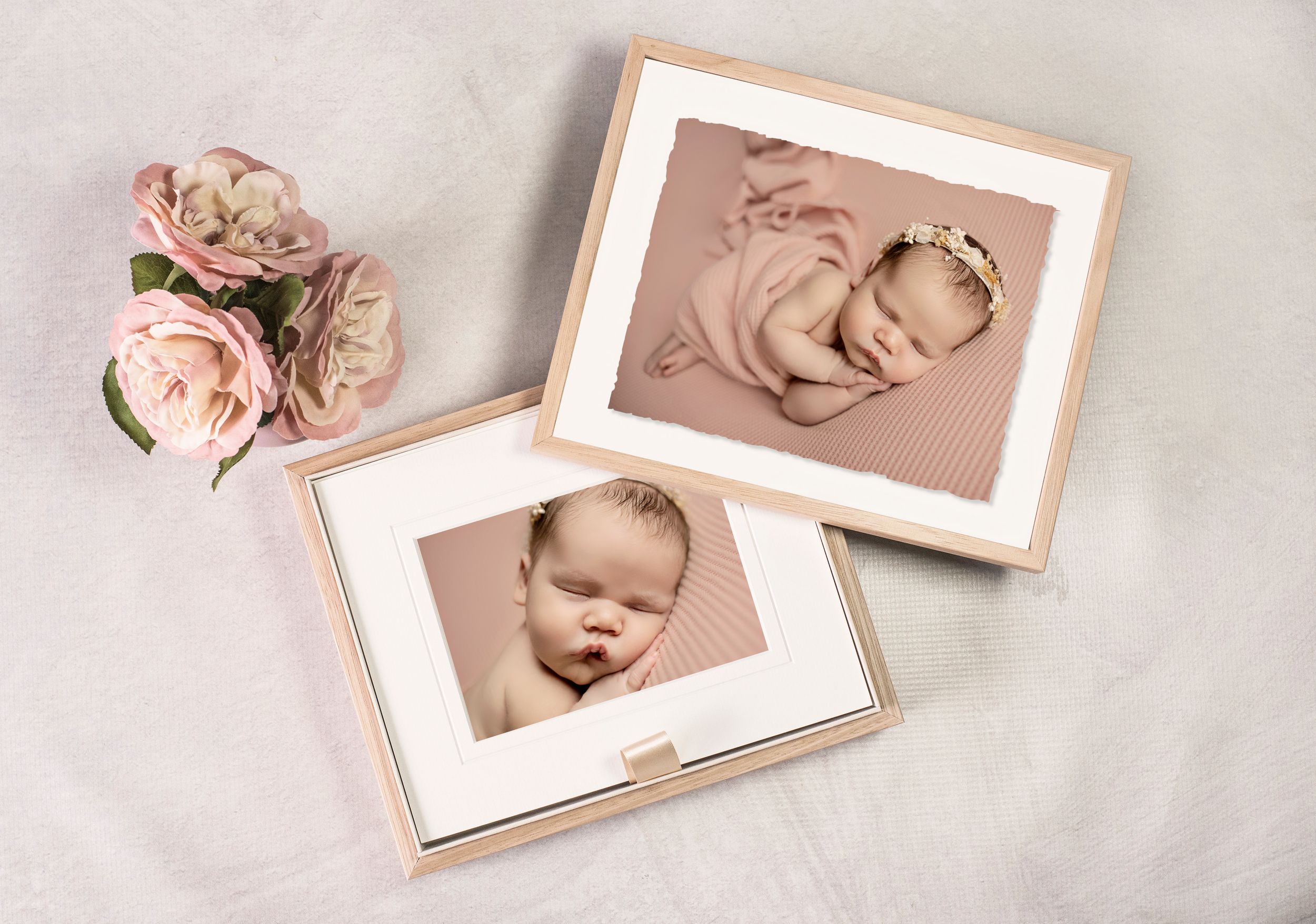 Two framed newborn baby photos displayed with pink roses, showcasing professional infant portrait photography in soft pink tones.