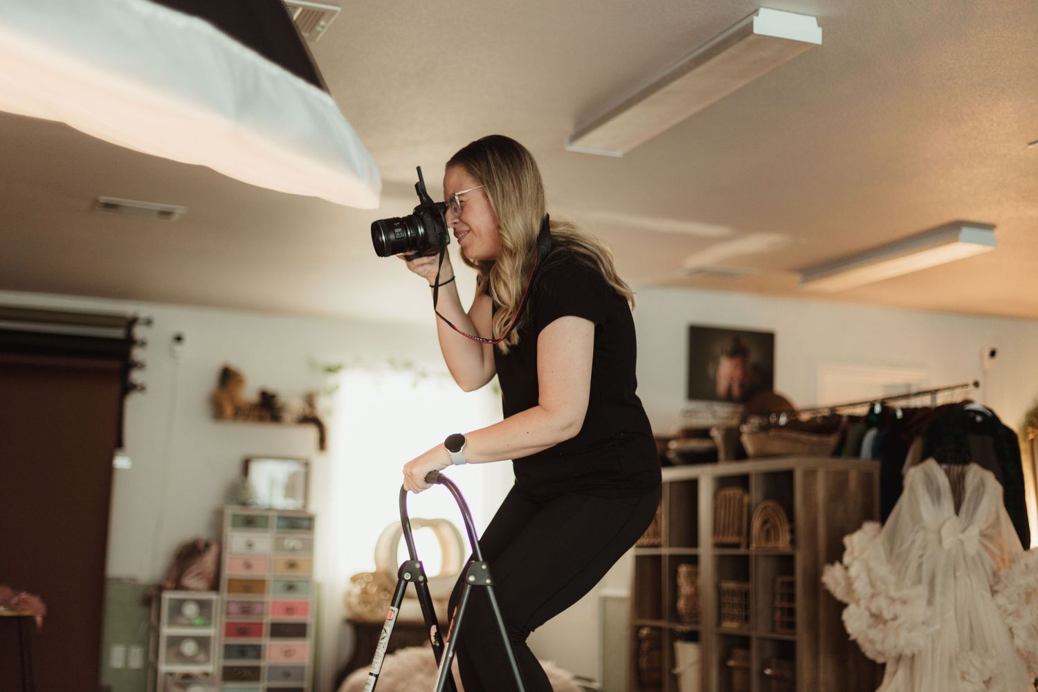 Photographer stands on ladder while shooting from high angle in studio setting.