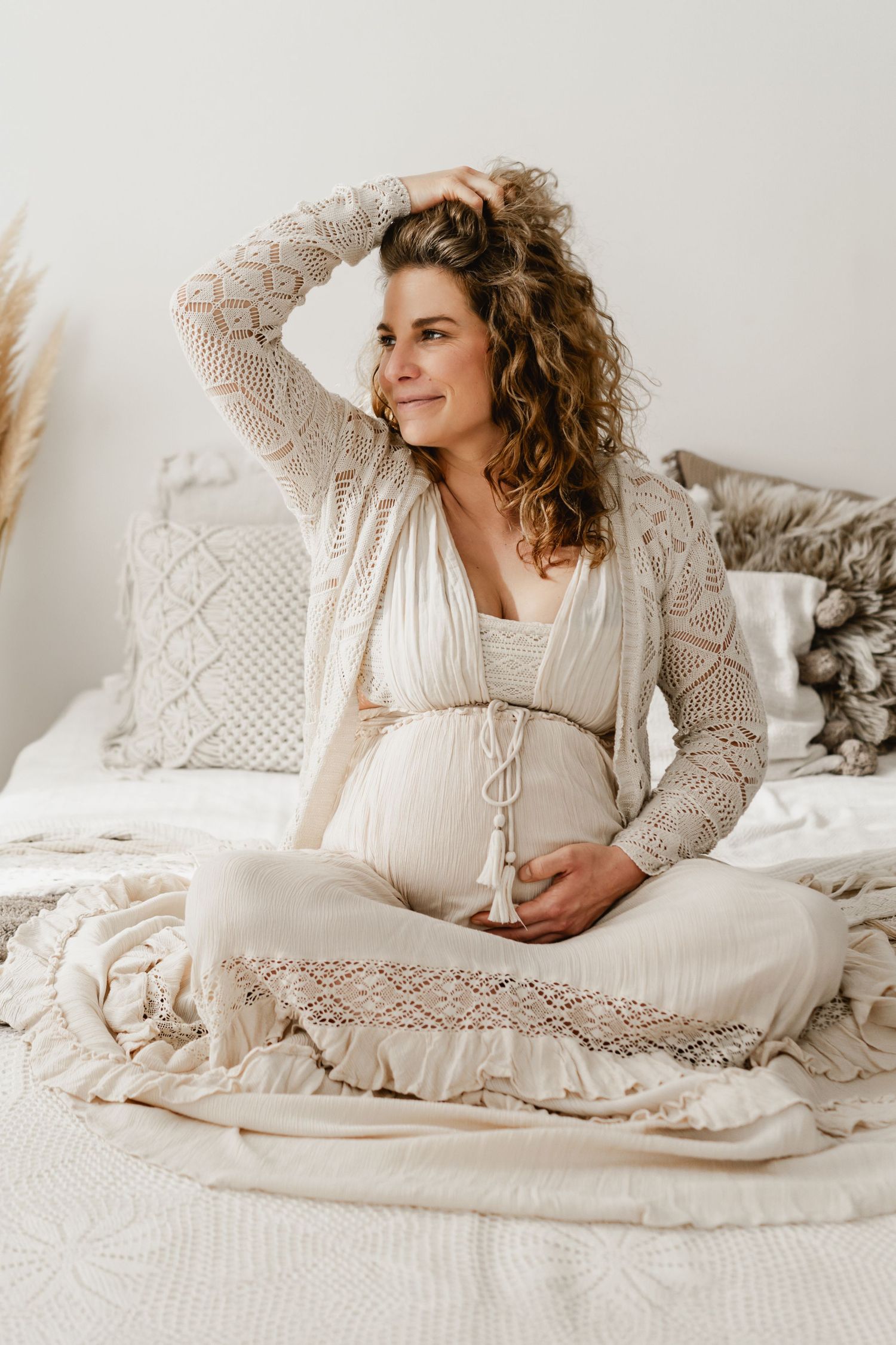 Schwangerschaftsfotos im Fotostudio Stockerau, die werdende Mama sitzt auf dem Shootingbett im Boho-Kleid