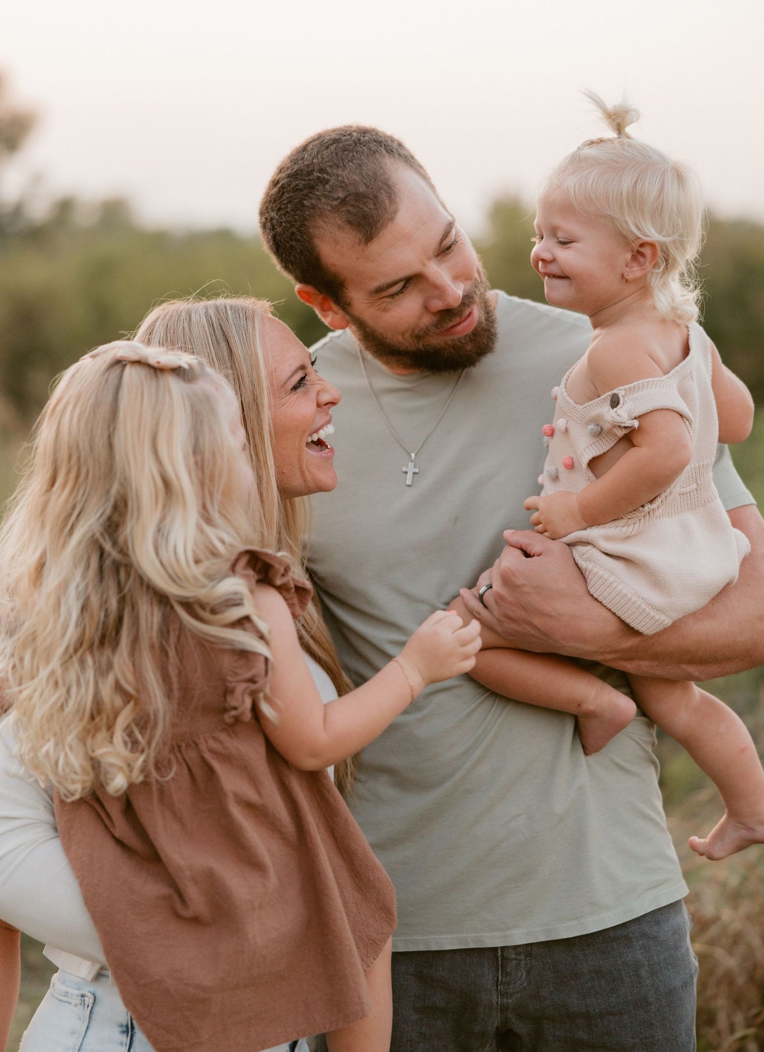 Happy young family with parents laughing and holding their smiling toddler outdoors in a golden field.
