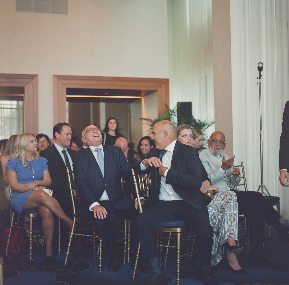 Group of elegantly dressed guests laughing and enjoying themselves at a formal indoor event or gala celebration.