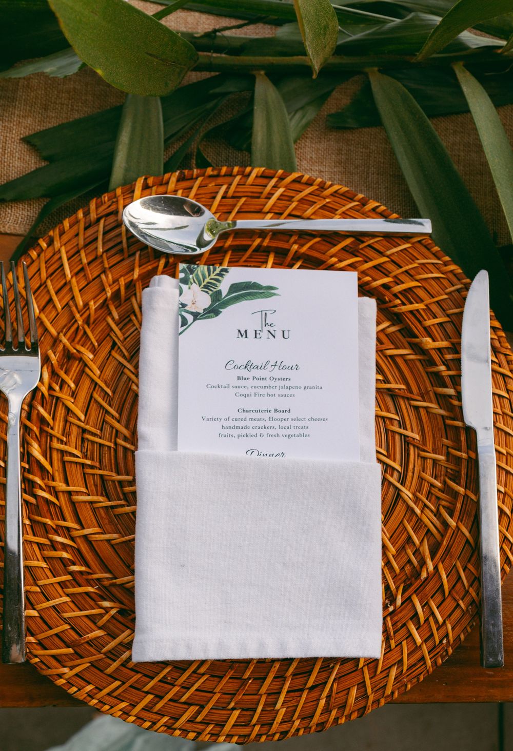 Elegant place setting with woven charger plate, white napkin, silverware, and a floral menu card on a rustic table.