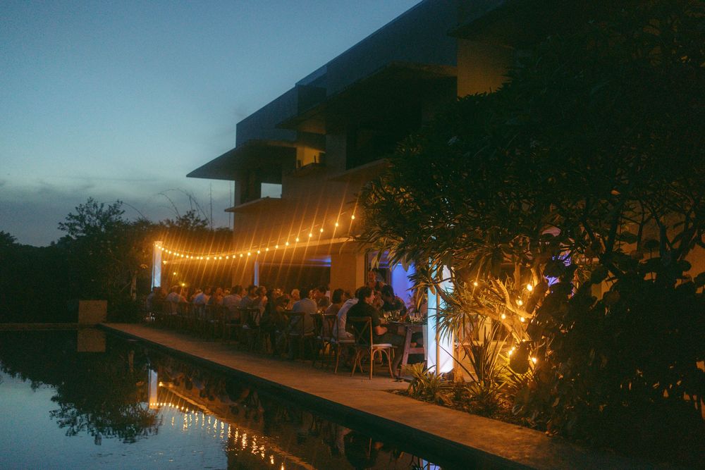 Outdoor evening event with string lights over a poolside dining area at dusk.