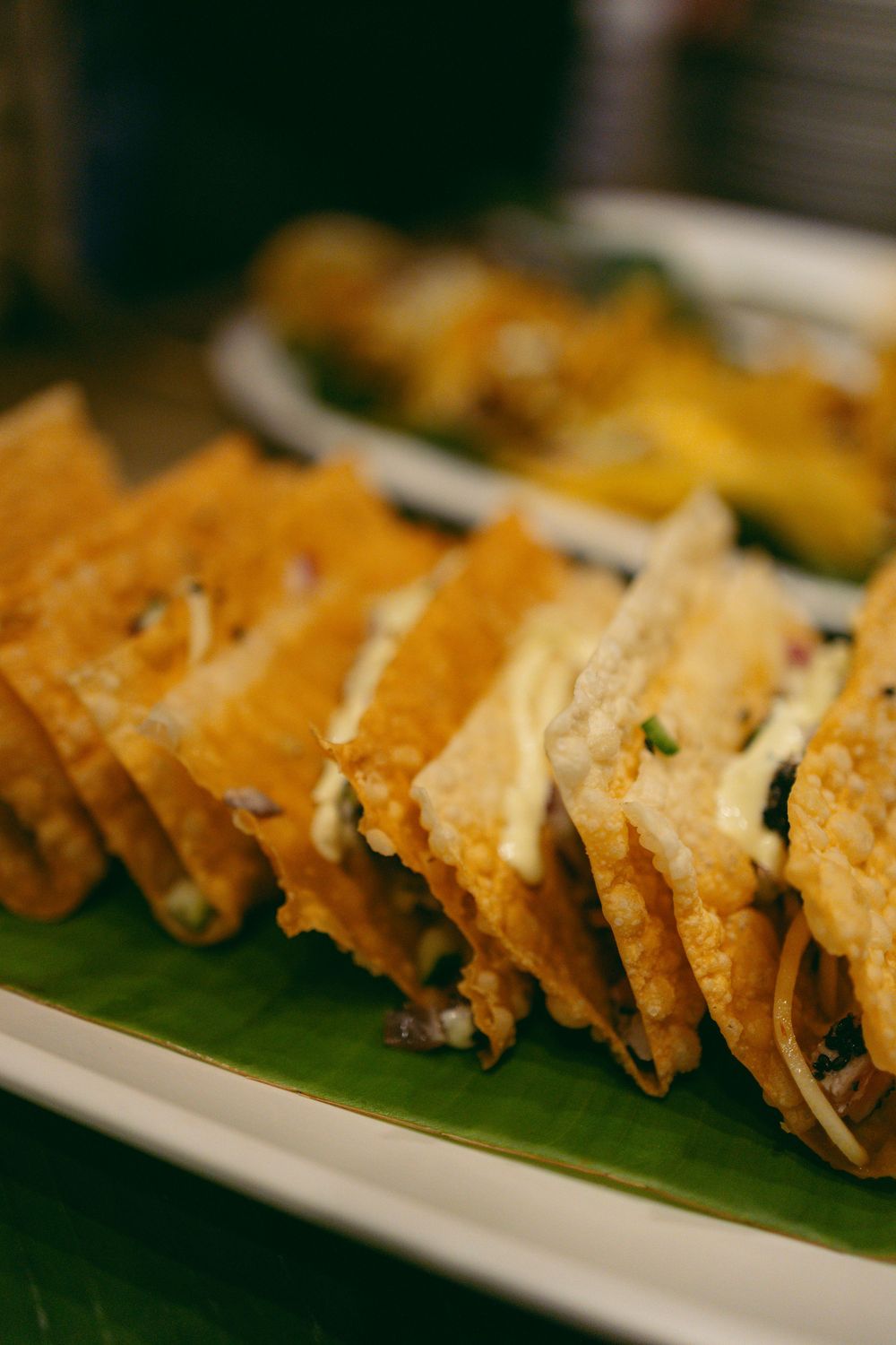 Golden crispy tacos filled with savory ingredients served on a banana leaf-lined white plate.