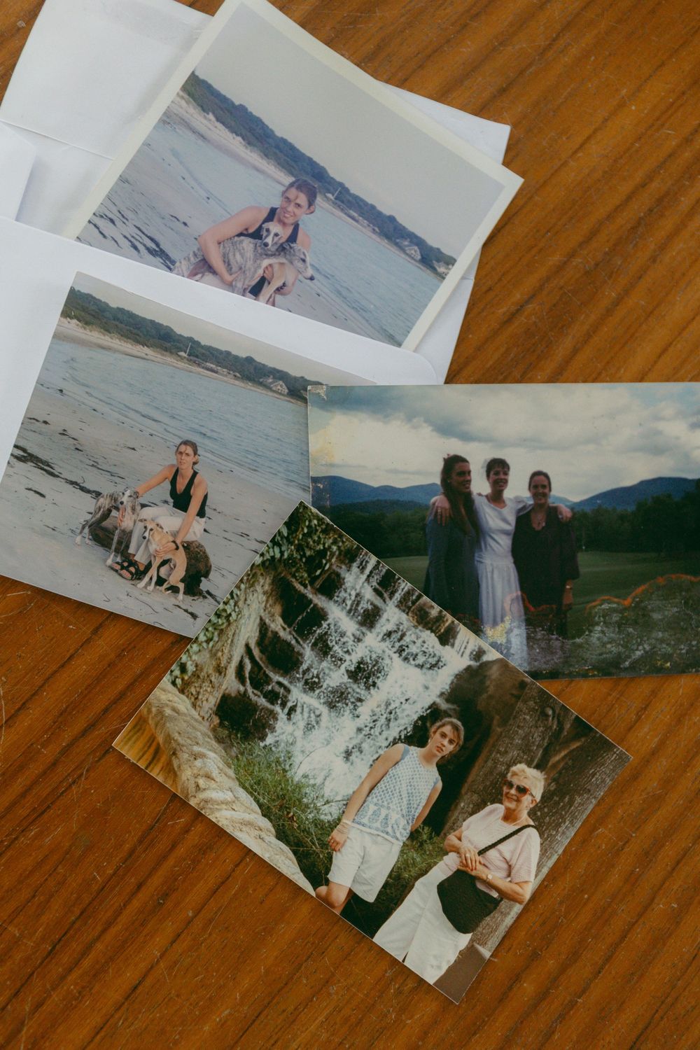A collection of four printed vacation photos spread on a wooden table, featuring beach and waterfall scenes.